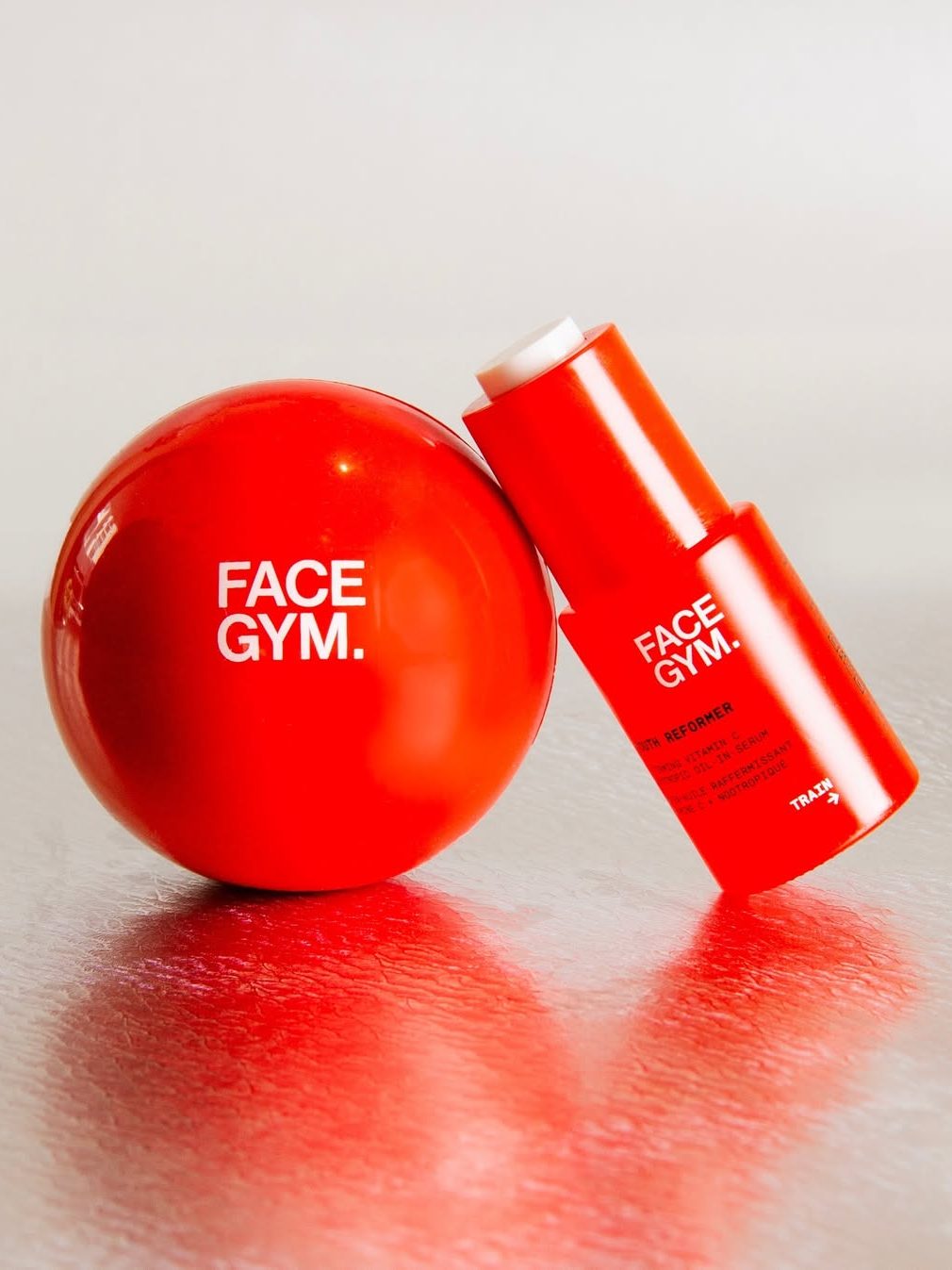 A red exercise ball and a skincare product bottle labeled 'FACE GYM.' on a reflective surface.