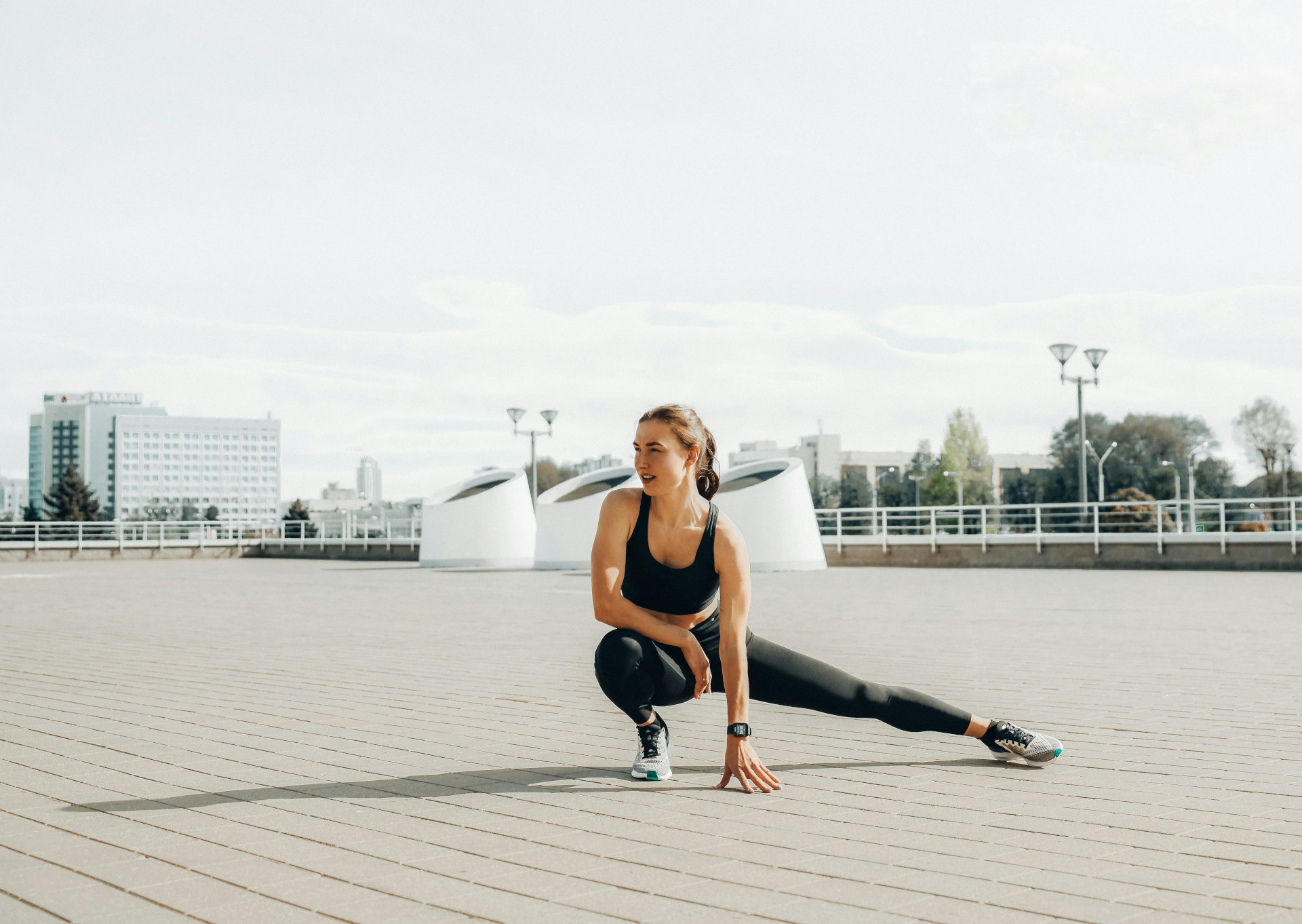A woman in activewear crouching in an athletic pose in a large, open, urban space