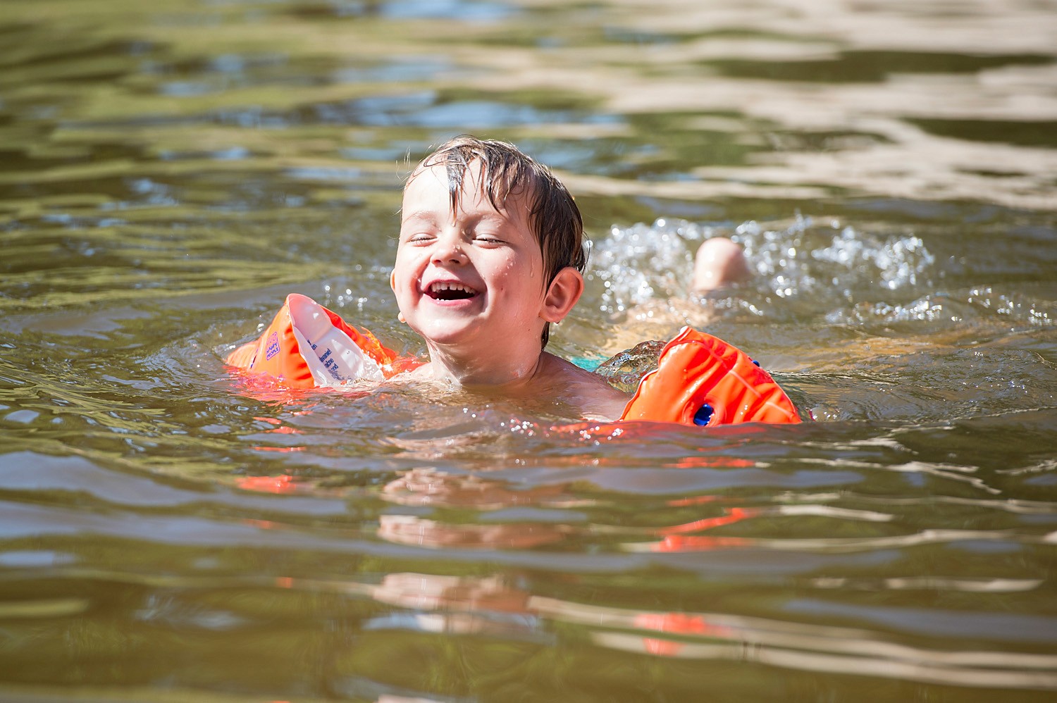 Kind mit Schwimmhilfe im Badesee am lachen