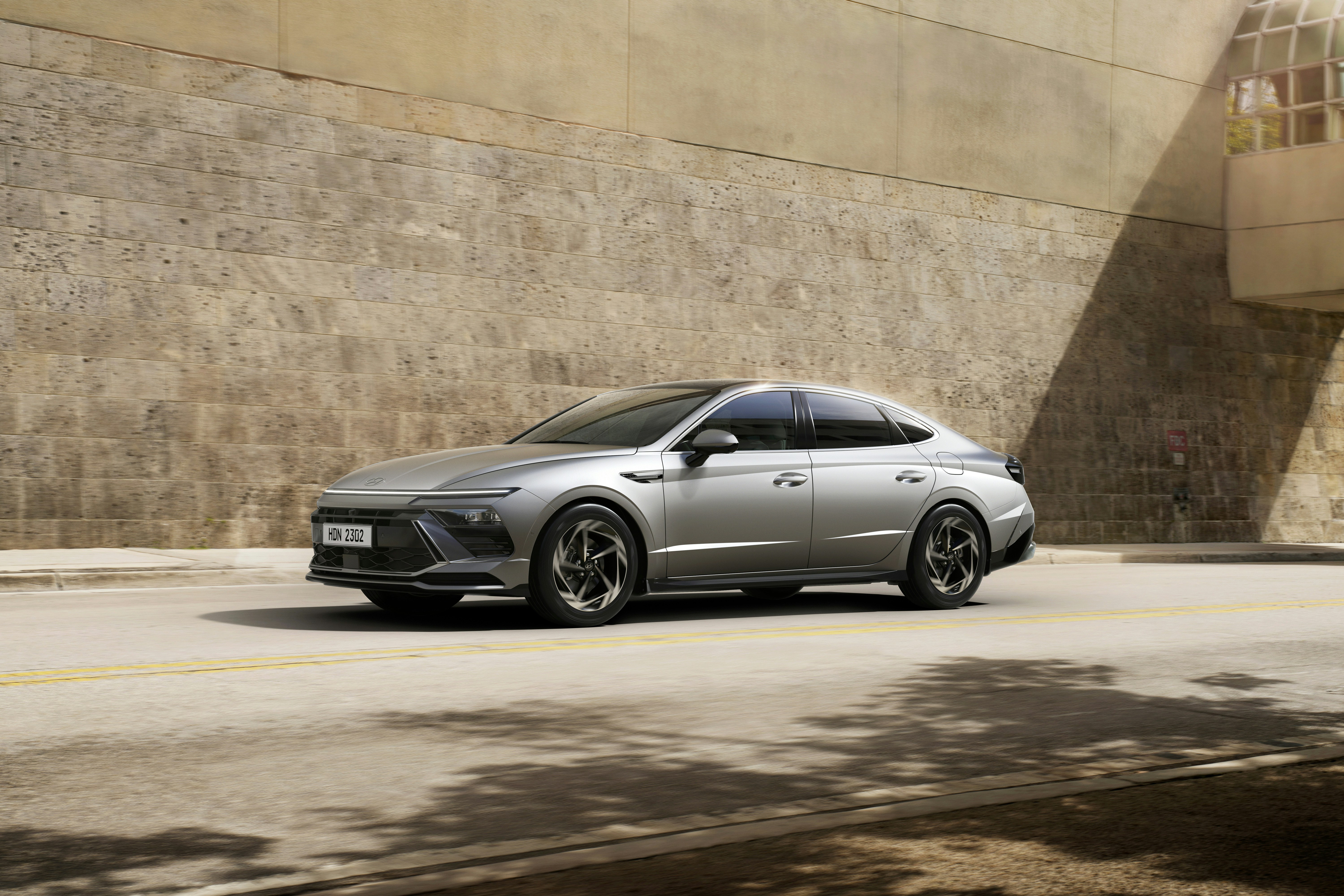 A silver car driving down a street next to a building