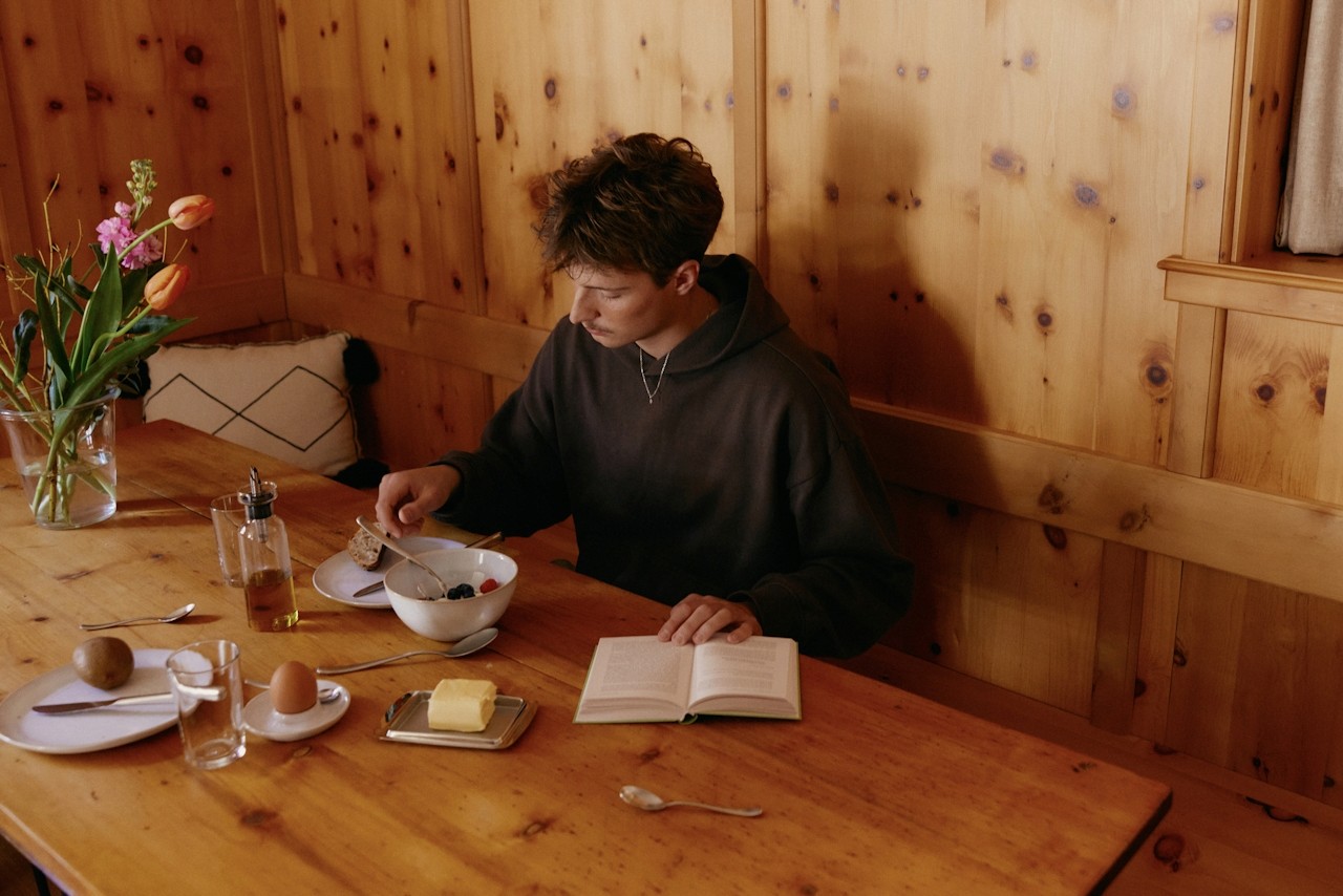 A person reading a book intently while simultaneously enjoying snacks nearby.