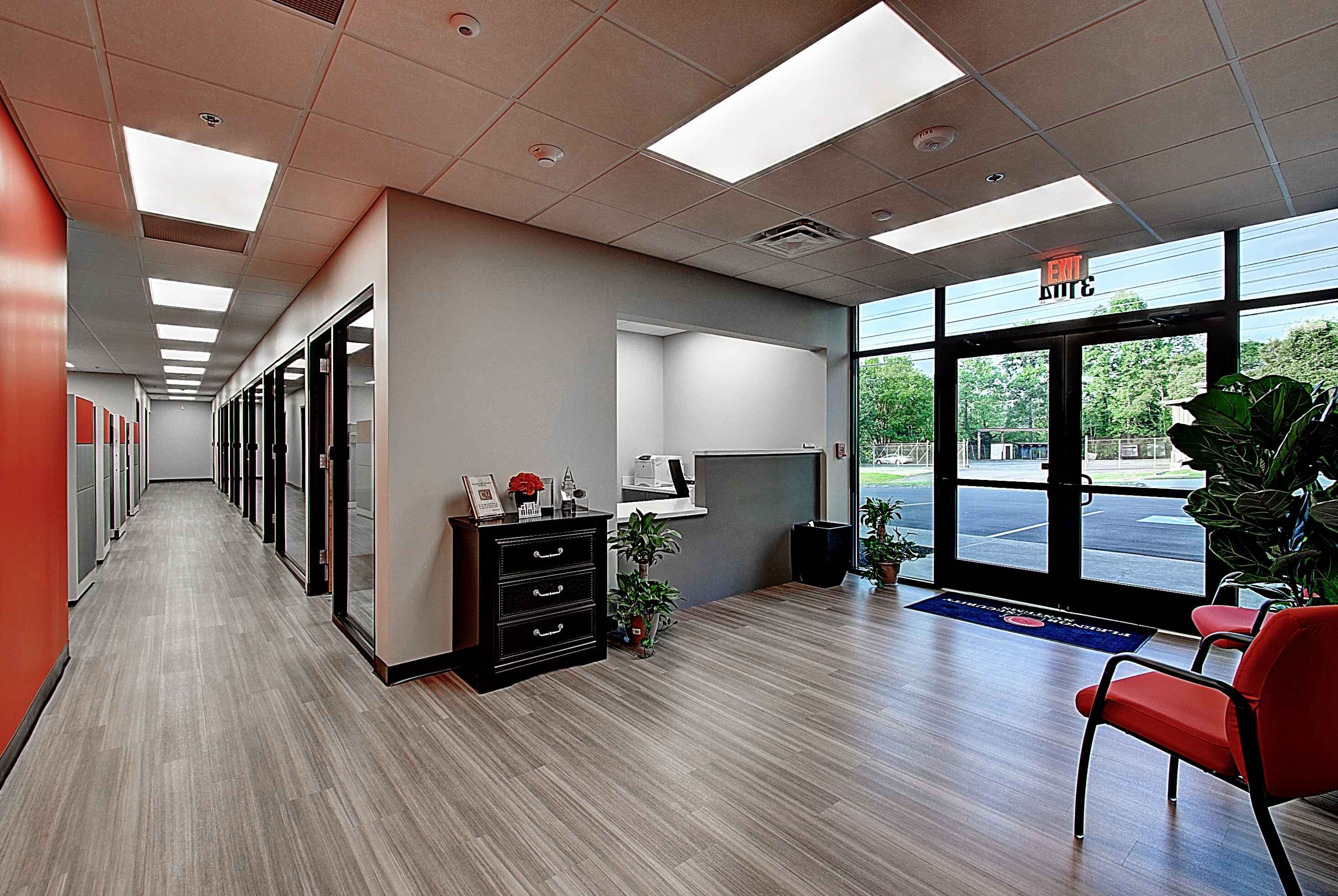 Modern office lobby with bright lighting, sleek furniture, and a view of exterior glass doors.