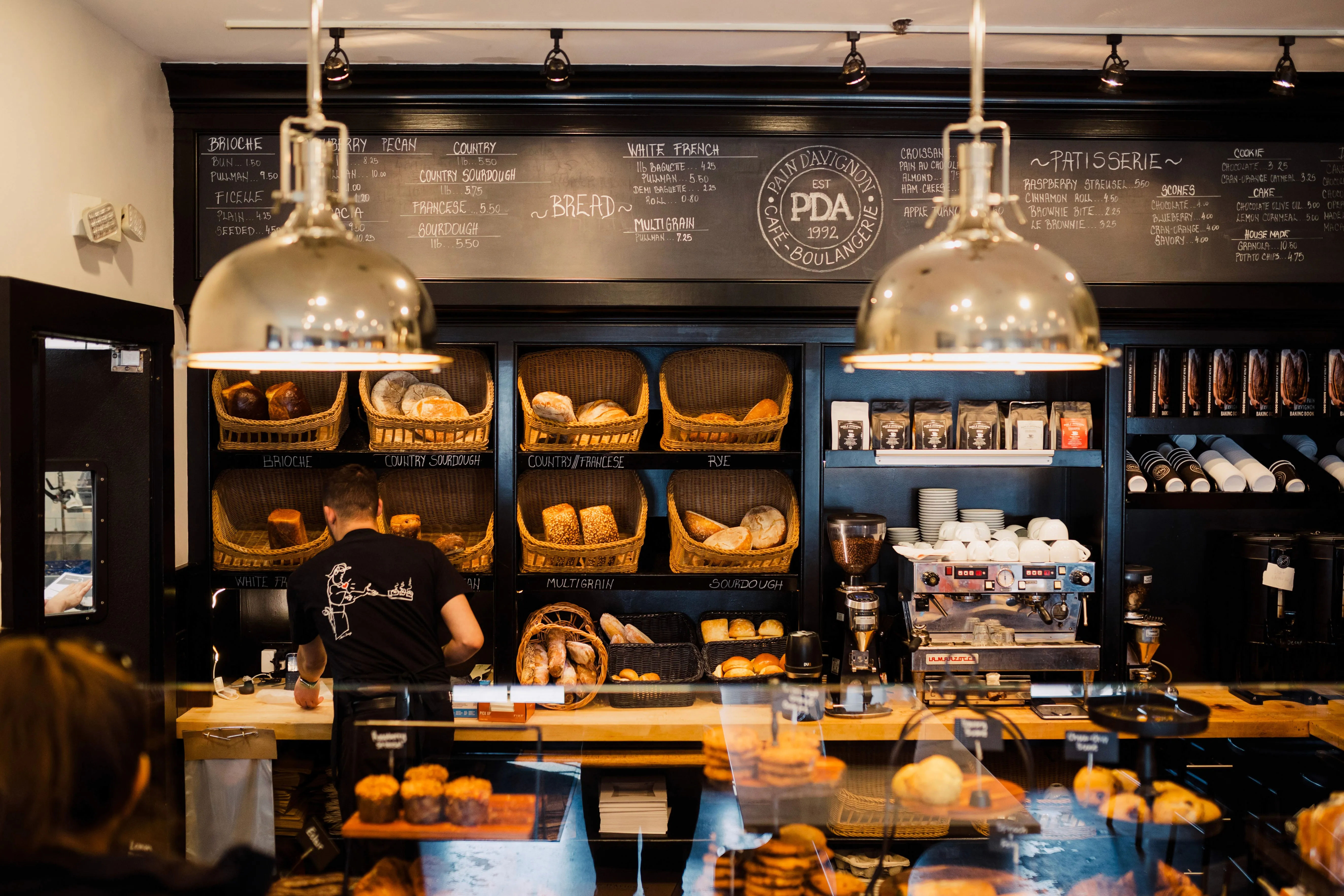 Inside Pain d'Avignon café Hyannis — espresso bar, fresh bread display and warm lighting at 15 Hinckley Road
