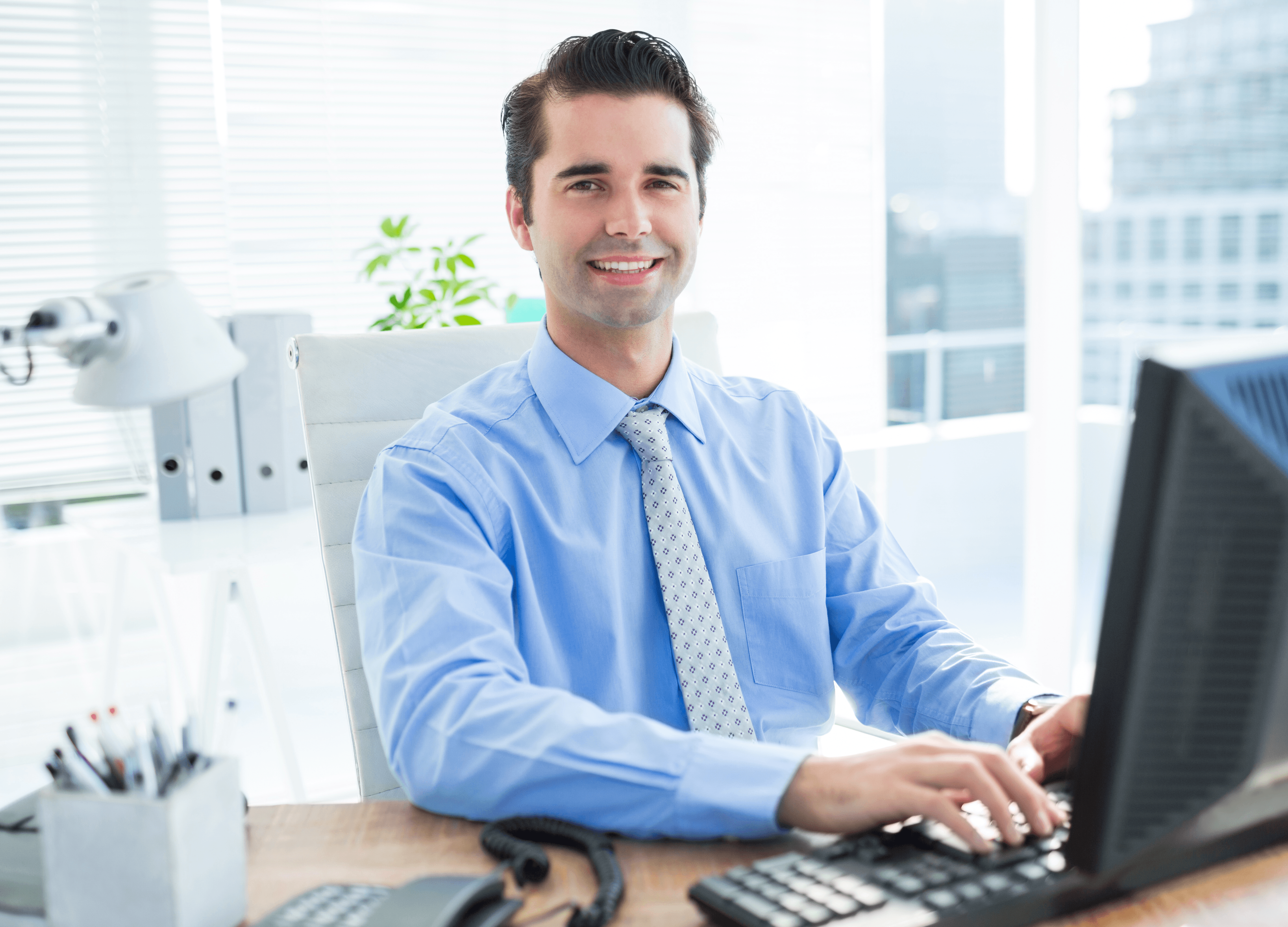 A smiling man engaged in a discussion with colleagues, gesturing while seated with a laptop in front of him