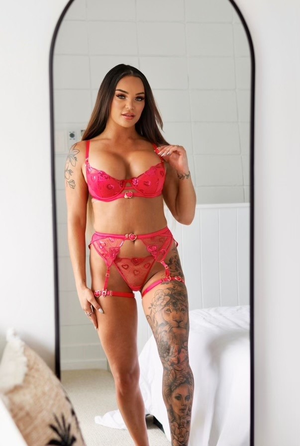 Topless waitress Mila posing in pink lingerie in a bright bedroom for an Hourglass Gold Coast promotional photo.