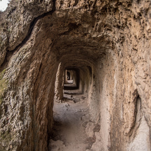 Un tunnel étroit aux parois rocheuses et irrégulières s'étend loin dans la distance, créant un effet visuel en couches.