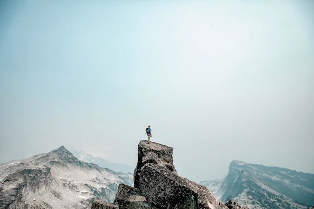 Person standing on a rocky peak above a foggy mountain landscape