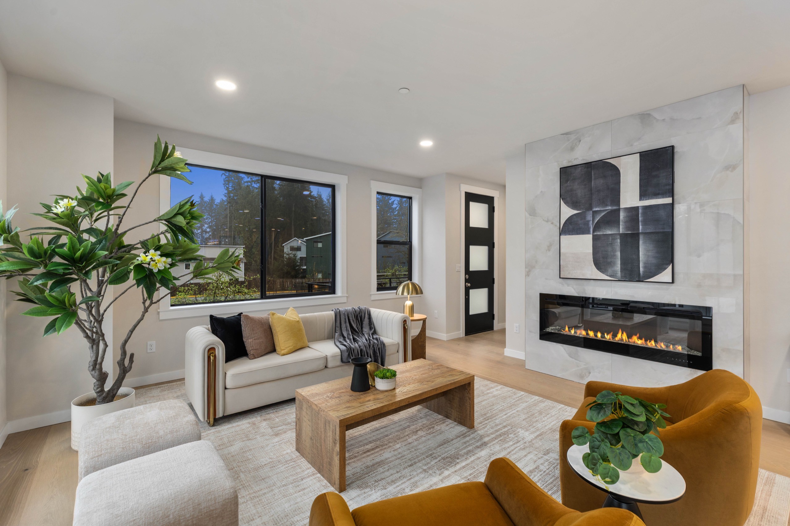 Spacious open-plan luxury living and dining area with linear gas fireplace, gold pendant chandelier, amber accent chairs, and designer wall art in a modern upscale home