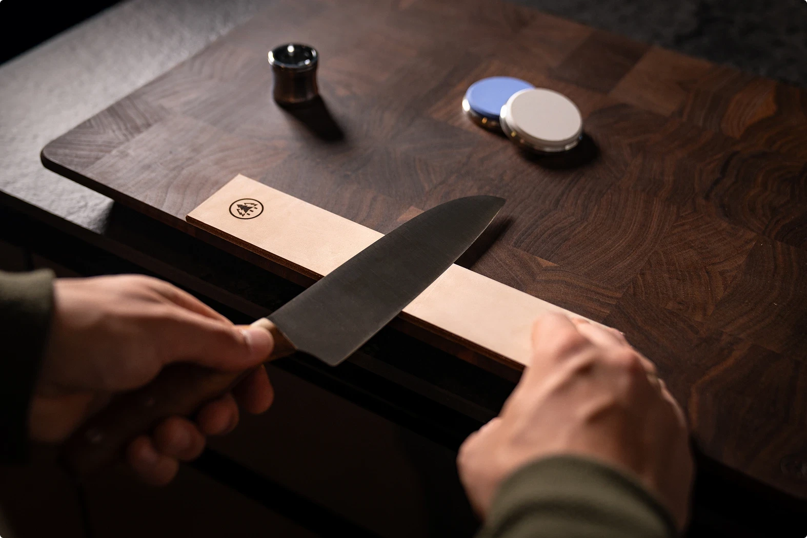 Drawing the knife blade across the leather strop while leading with the spine to refine the edge.