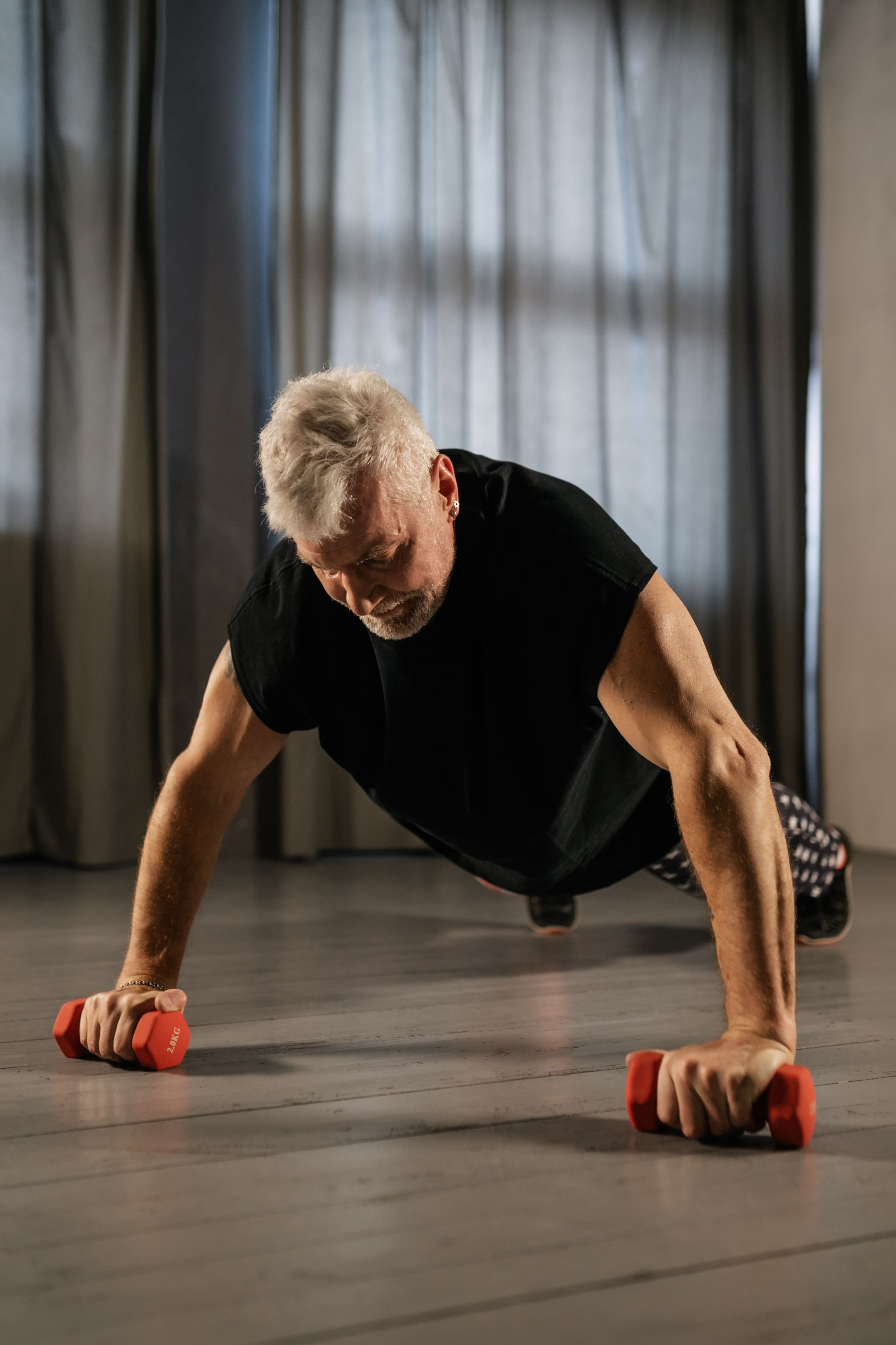 elderly-man-performing-a-plank-exercise-indoors-using-red-dumbbells-for-strength - alena-darmel (pexels)