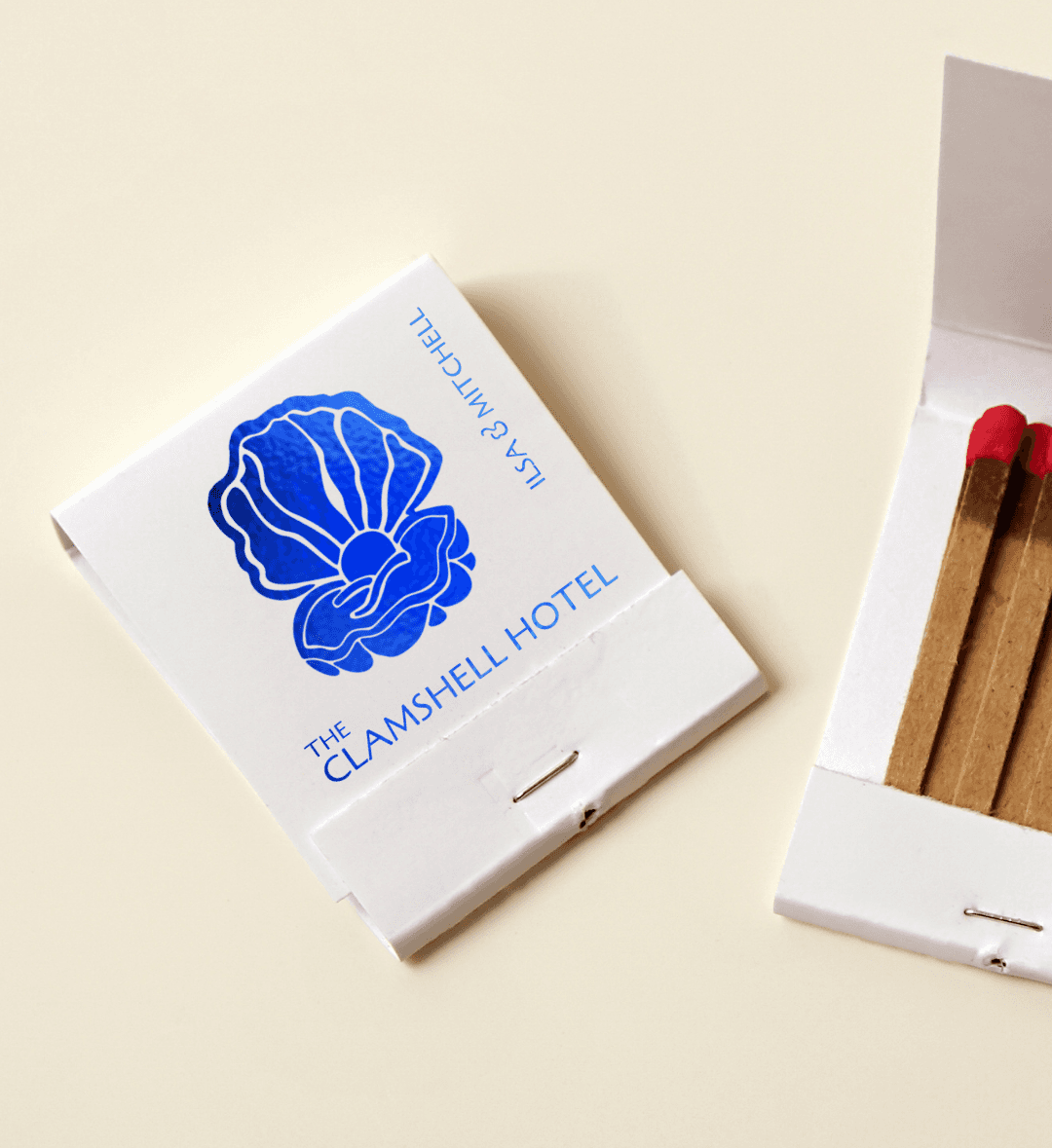 an eggshell colored matchbook with an abstract irridescent blue clamshell design on the center and the text "the clamshell hotel | Ilsa & Mitchell”