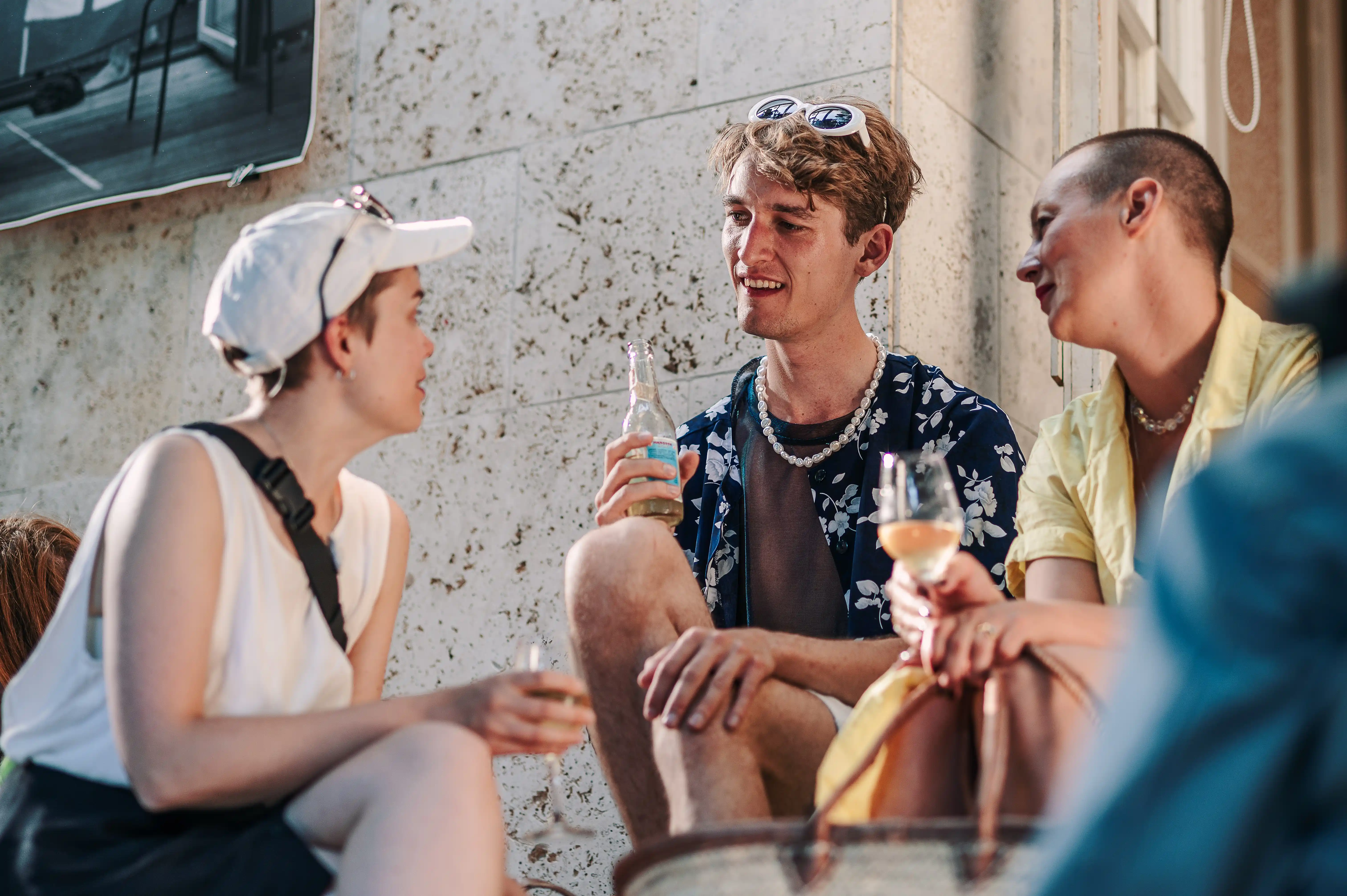 Unge kulturgængere drikker champagne mens de sidder på kantsten.