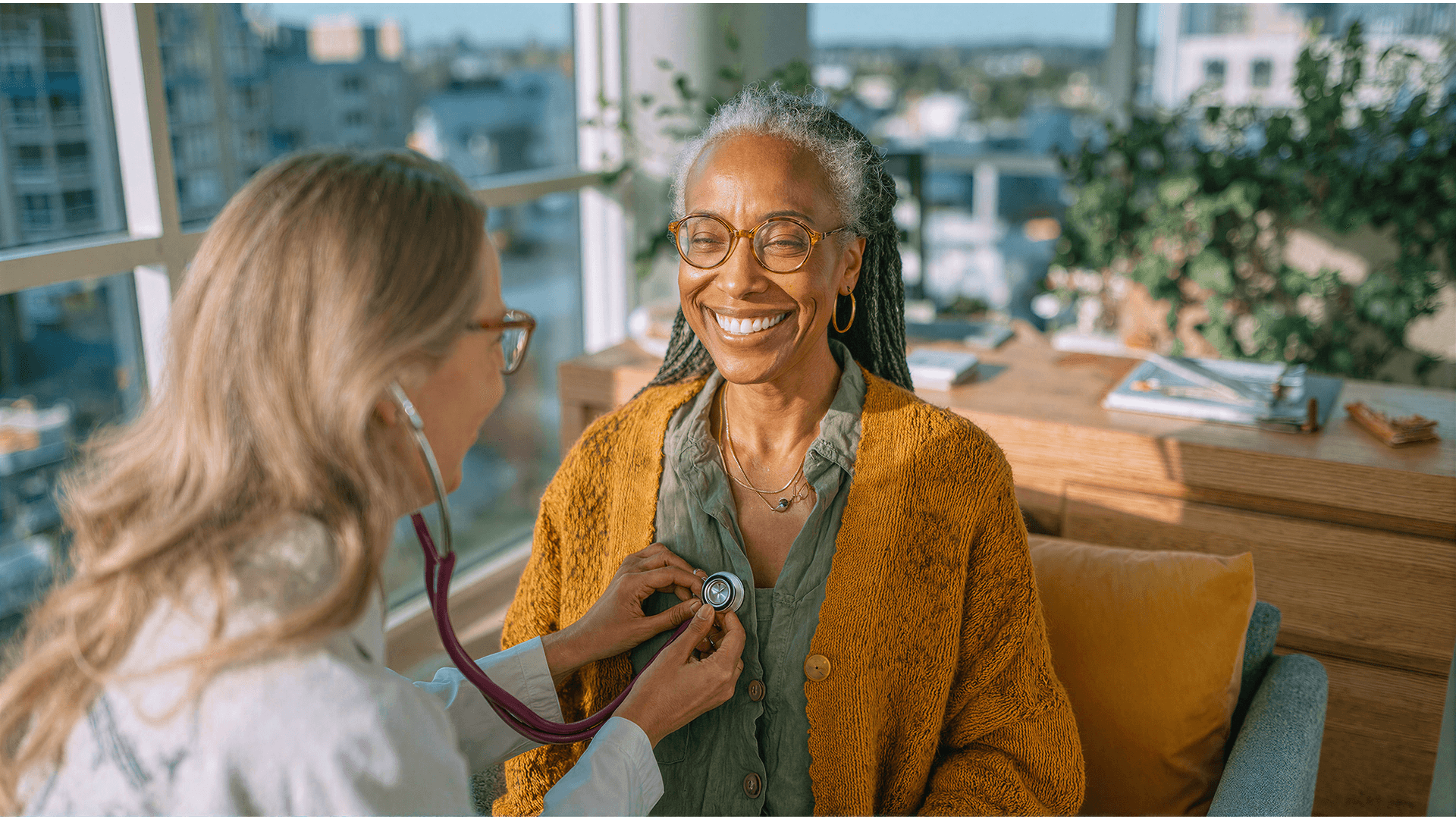 Profissional de saúde usando estetoscópio em paciente sorridente durante consulta em ambiente iluminado e acolhedor, como as clínicas que a Tivita atende.