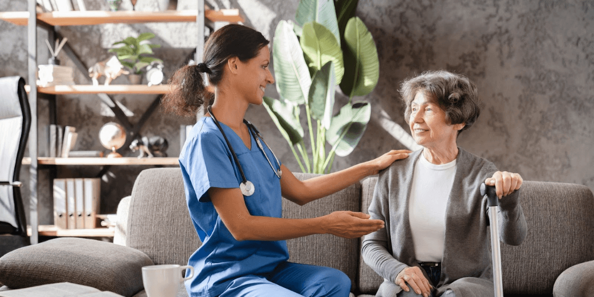 Image ALT Text Generator said: Smiling senior woman chatting with caregiver in a bright common room, representing the choice between day care and assisted living.