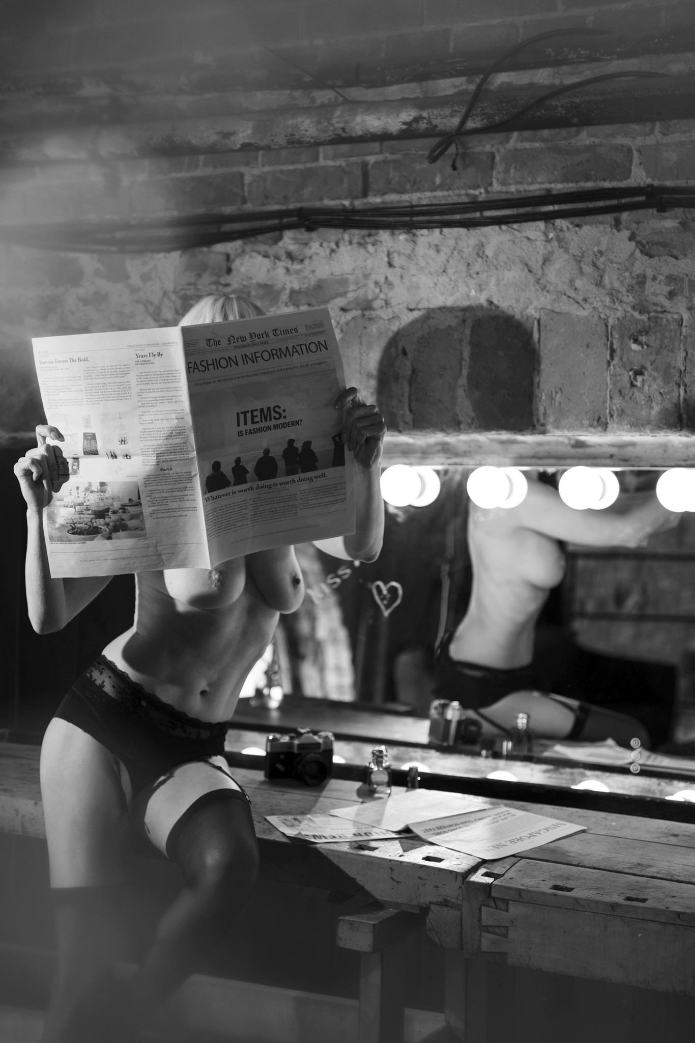 Woman reading a newspaper, dressing table with lights in the background - The Space Between Roles - Agnieszka Czyzkowska Photography