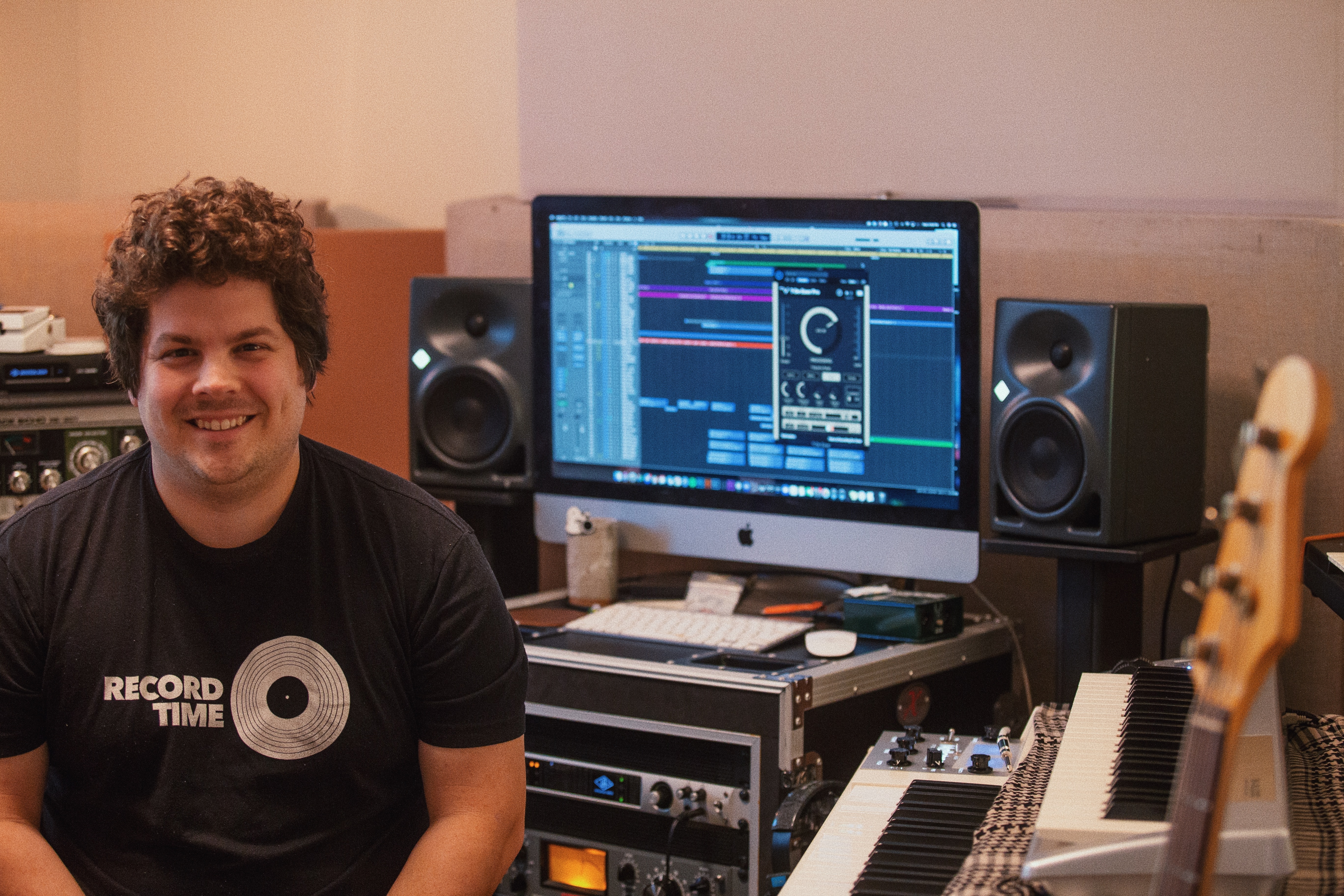 man smiling with music setup in background - how to write a song for beginners