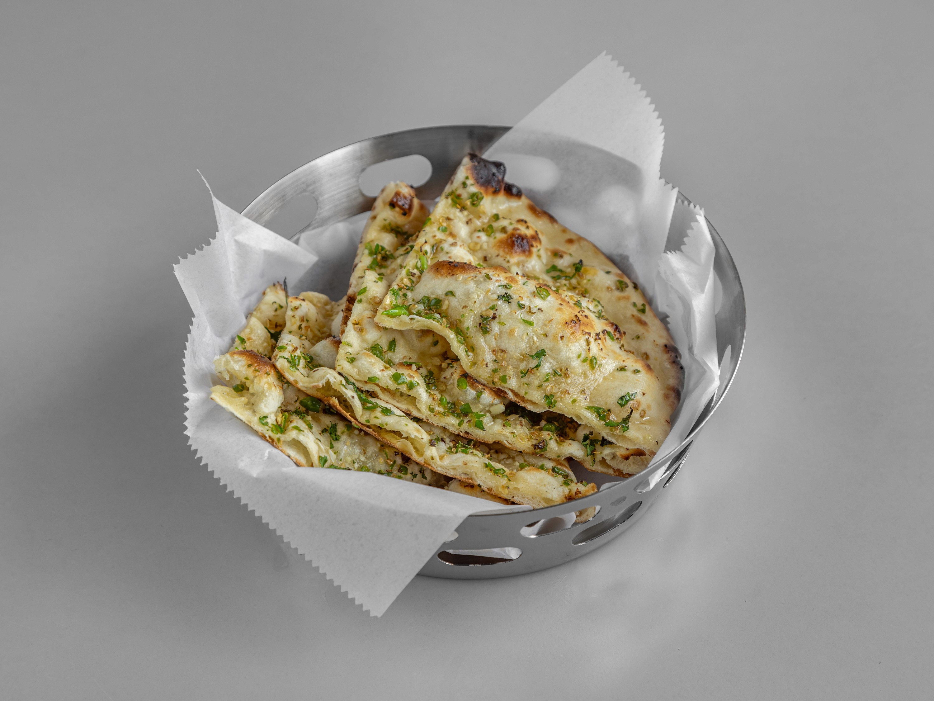A close-up shot of a fork twirling strands of creamy white pasta, possibly carbonara or cacio e pepe, heavily garnished with dark black pepper or truffle shavings, against a stark white background.