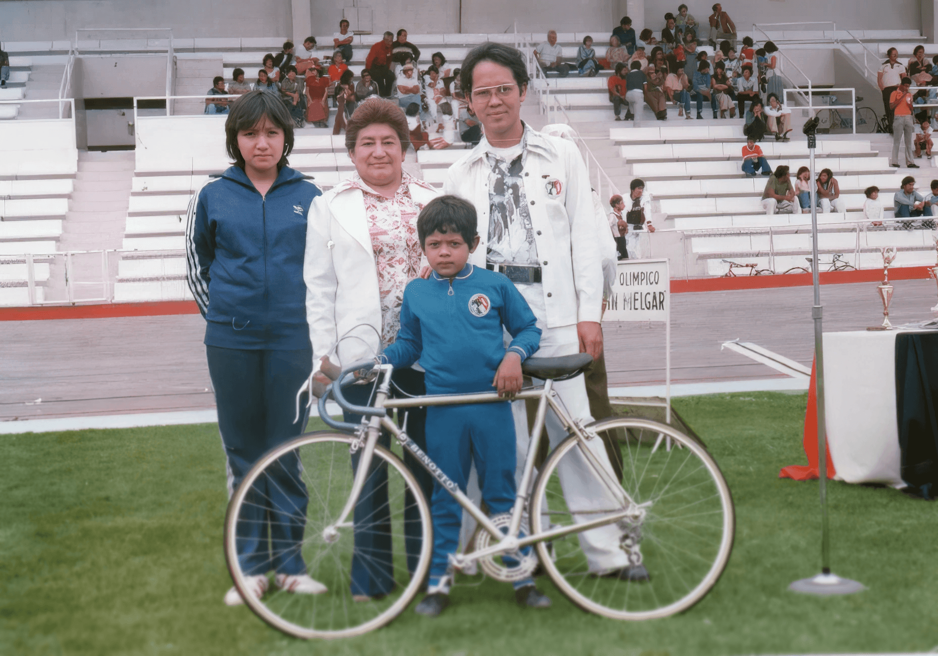 Marco Navarro de niño posando con su bicicleta y su familia en el velódromo Agustín Melgar durante evento de ciclismo infantil.