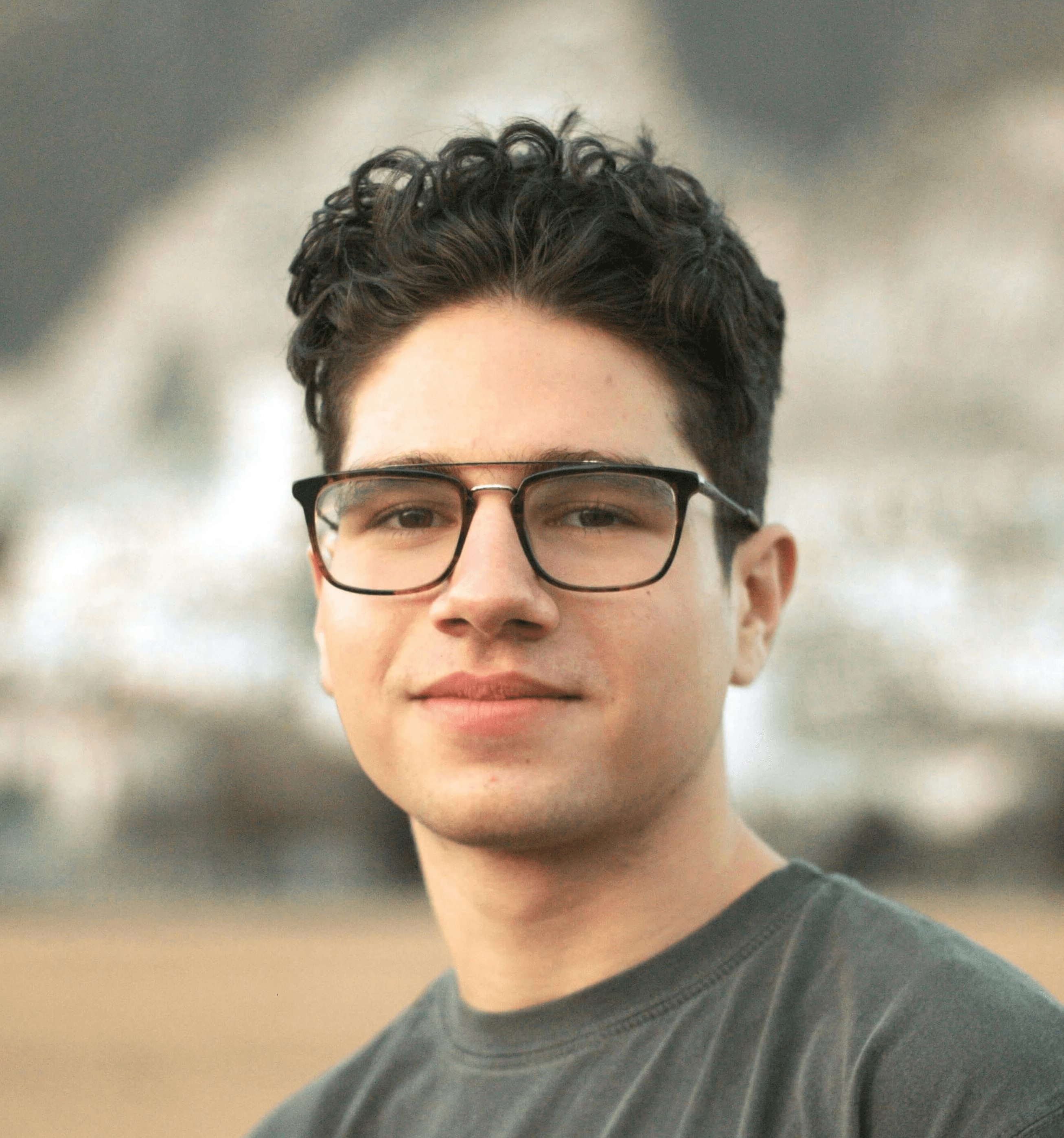 a young man wearing glasses standing in front of a mountain