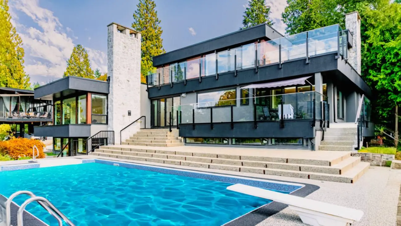 Luxury custom home rear exterior featuring modern architecture, multi-level design, glass railings, inground pool, and stone terrace built by Vancouver Custom Homes