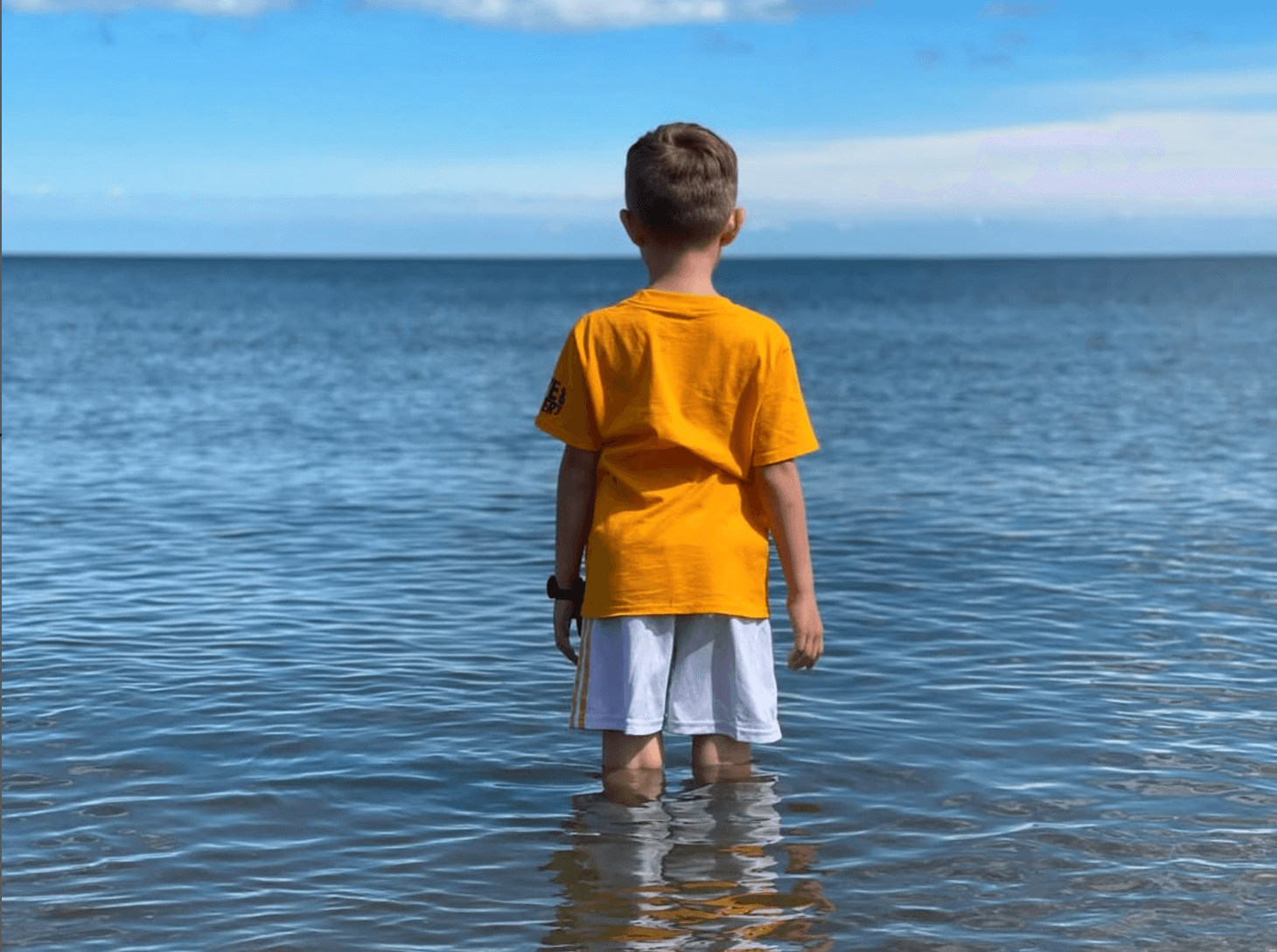 Boy stanging in shallow ocean water looking out to the horizon 