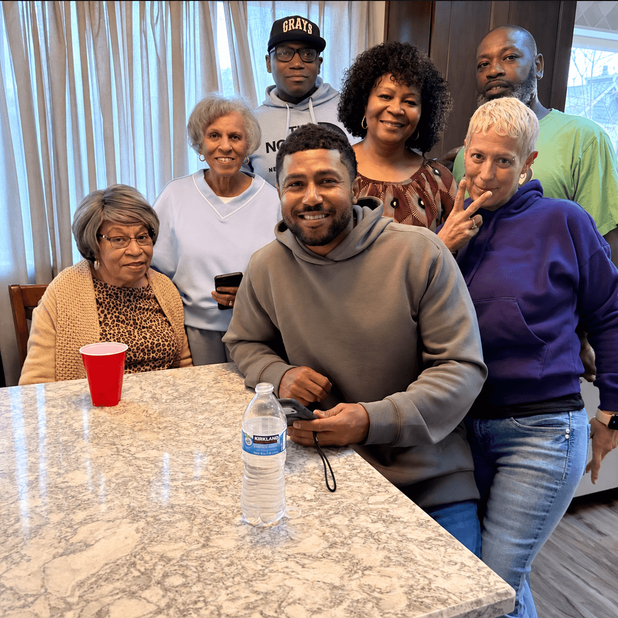 Seven people gathered indoors around a table for a casual group portrait.