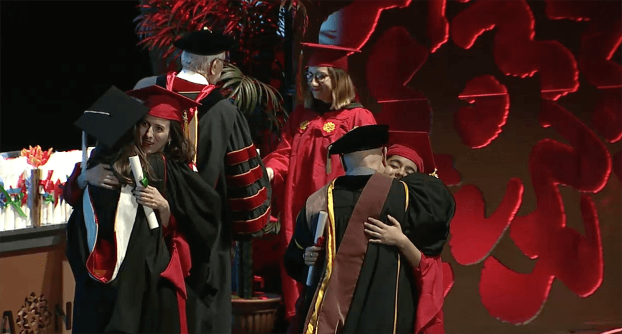 A photo of a couple of grad students and teachers hugging and congratulating each other.