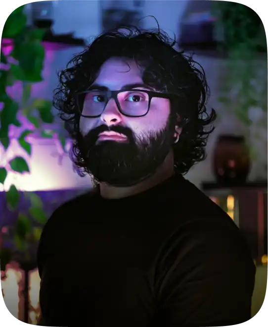 Foto di Claudio Ragusa in uno studio attorniato da luci di vari colori, in un'atmosfera calda e pacifica. Sullo sfondo alcune piante.