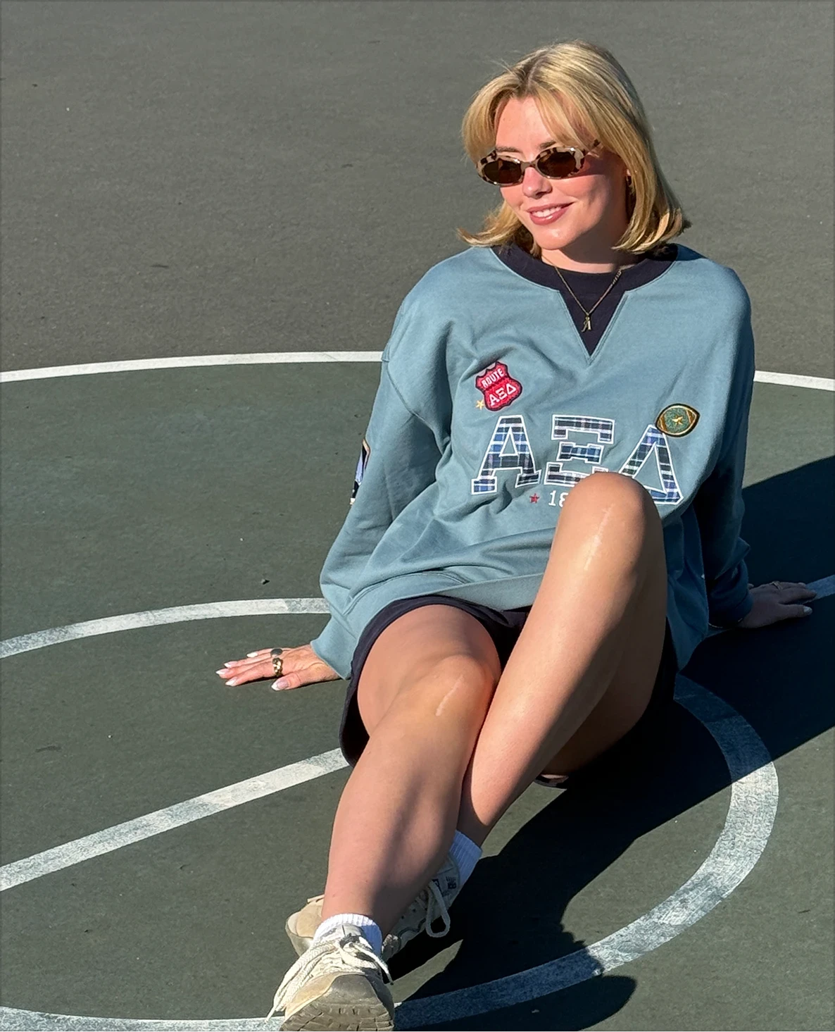 AXID's Izzy Murphy seated on an outdoor court wearing a teal retro crewneck and navy shorts.