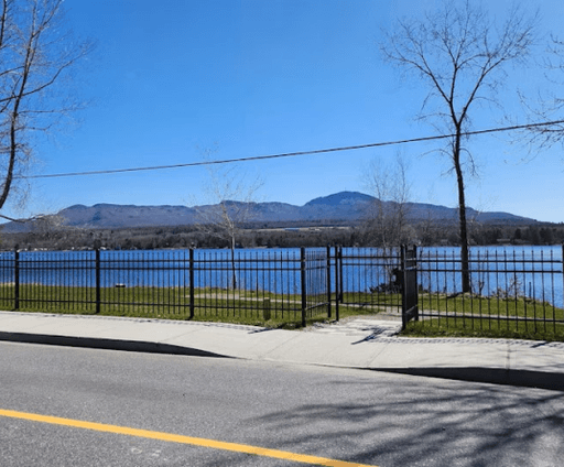 Vue sur le lac d’Argent et les montagnes à Eastman, prise depuis la route bordée d’une clôture noire et d’un trottoir.