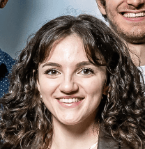 A smiling young woman with dark curly hair, part of the dynamic PointOne team developing innovative digital product.