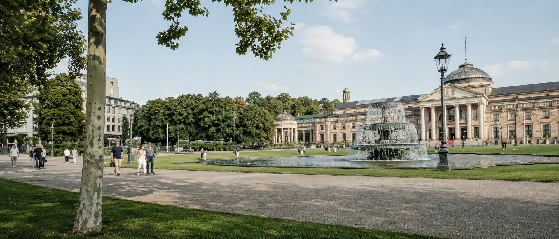 Wiesbadener Kurpark mit Spaziergängern, Brunnen und Kurhaus im hellen Tageslicht