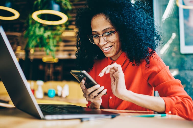 Smiling woman using smartphone while working on laptop