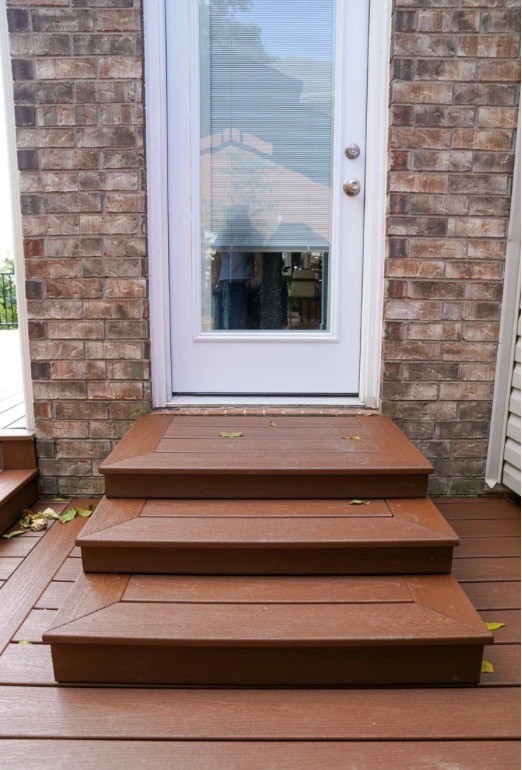 A modern hallway features vibrant teal and orange geometric and leaf patterns, with glossy tiled floors, a large rectangular light fixture, and a small shelf holding a potted plant, all leading to a large, frosted window at the end.