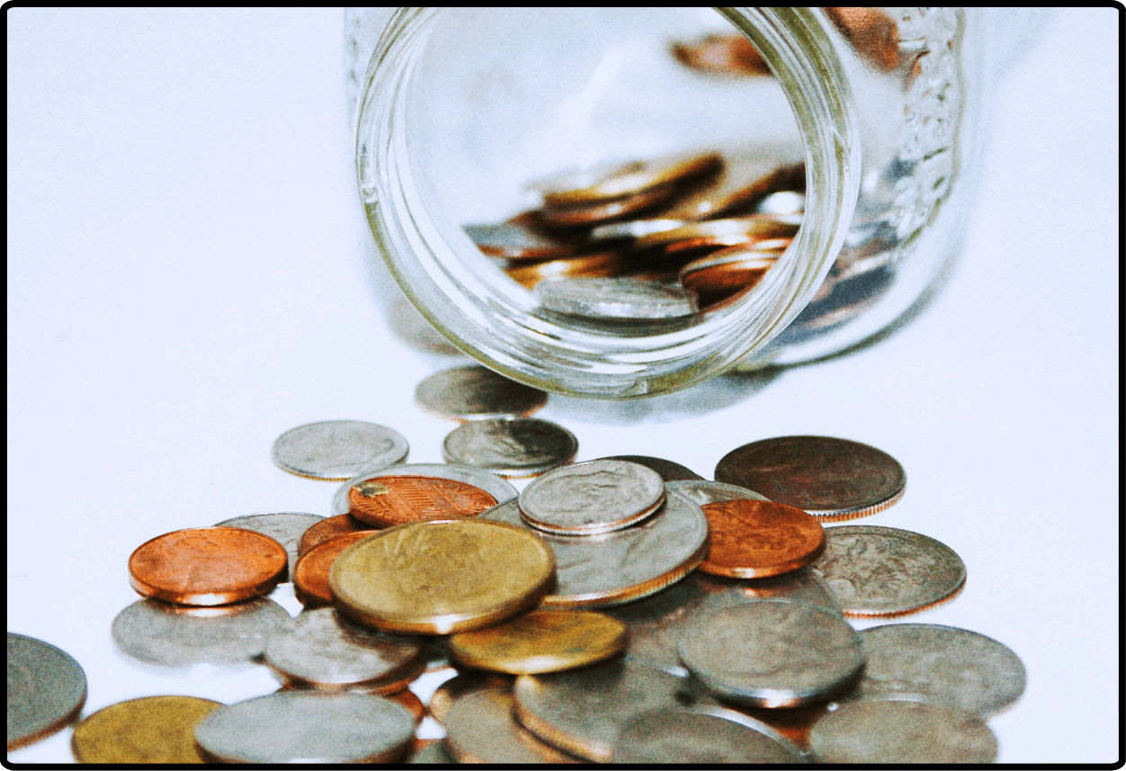 A glass jar spilling out several coins