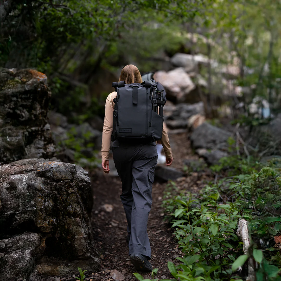 Woman walking through trail wearing black backpack