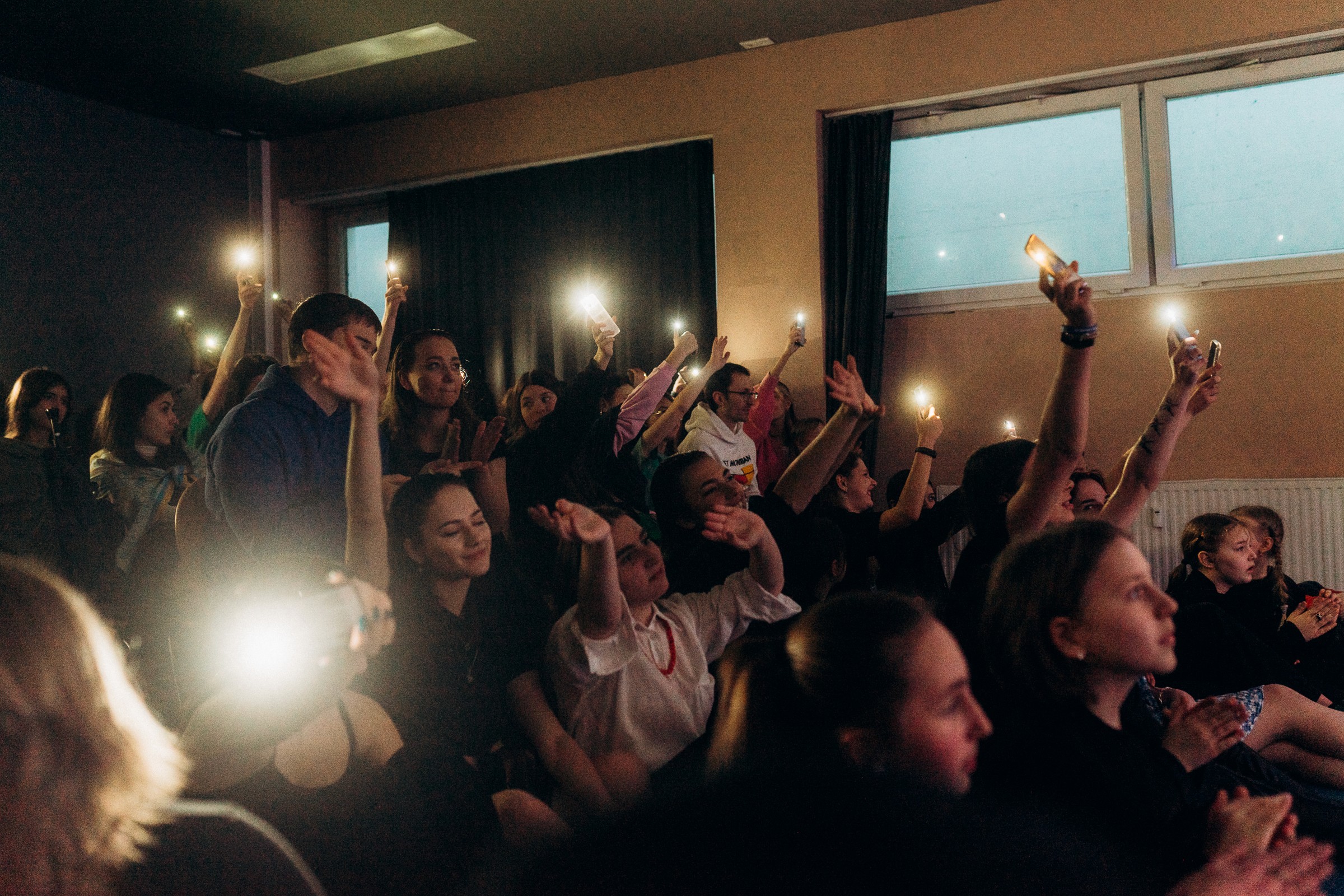 Das Publikum sieht sich ein Theaterstück an und hält dabei seine Handys mit eingeschalteten Lichtern über den Kopf, um die Szene zu beleuchten.
