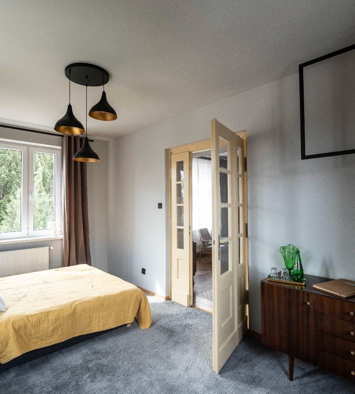 Łóżko z żółta narzutą w Villi Stara Apteka. Noclegi dla grup w Srebrnej Górze