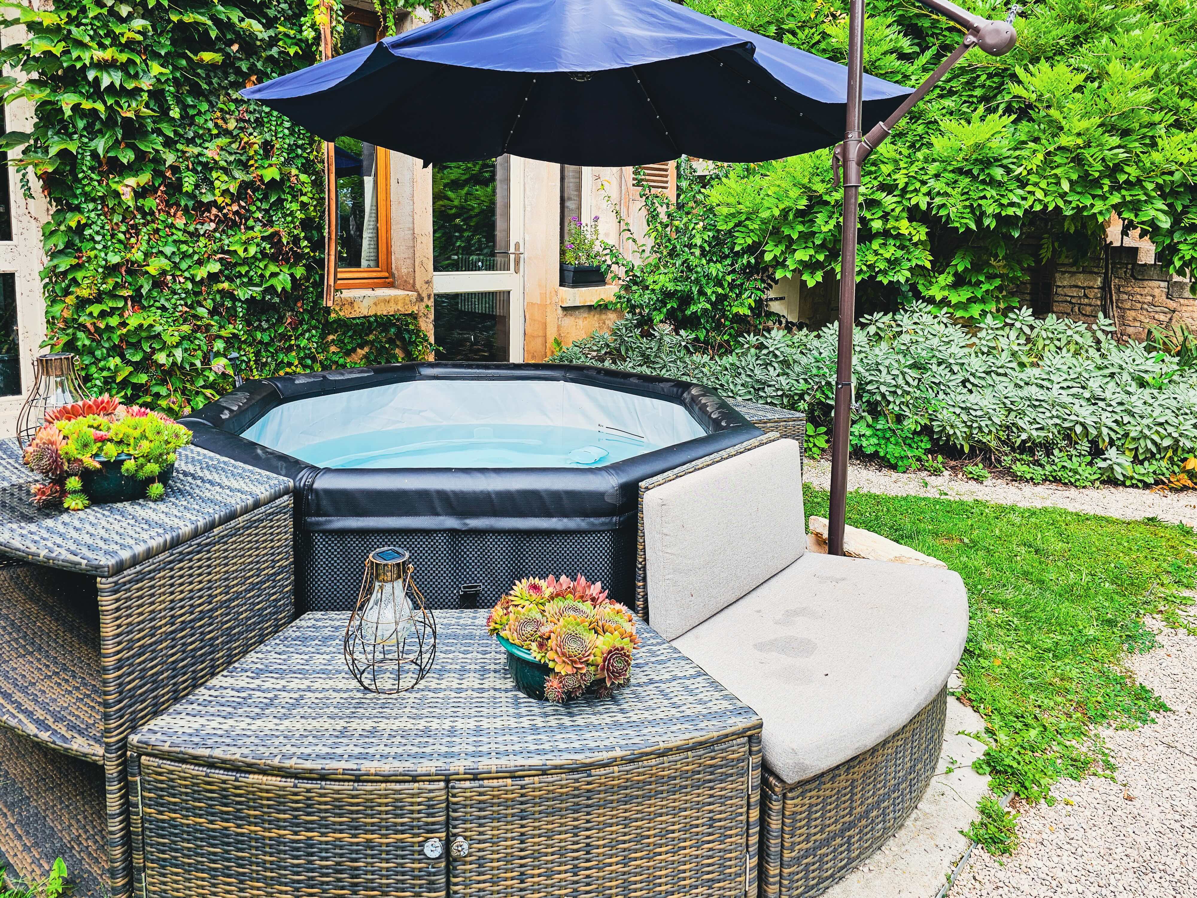 Jacuzzi extérieur dans jardin verdoyant avec parasol bleu. Détente et relaxation.