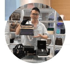 The image shows a person in a store holding a luxury handbag, with other designer bags displayed on the counter.