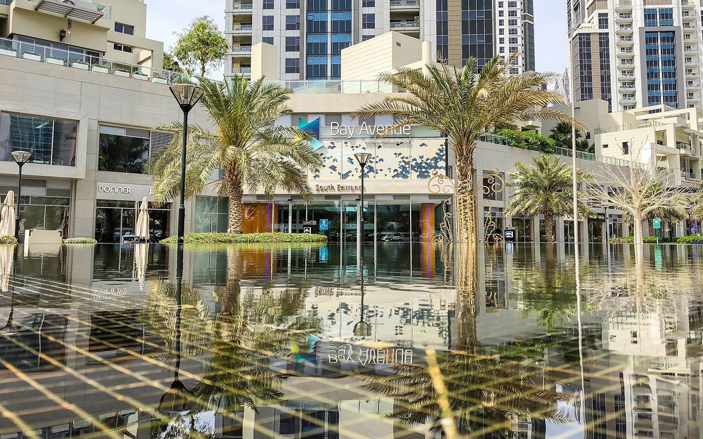 Palm trees and shops at Bay Avenue in Business Bay with reflections in a shallow water feature