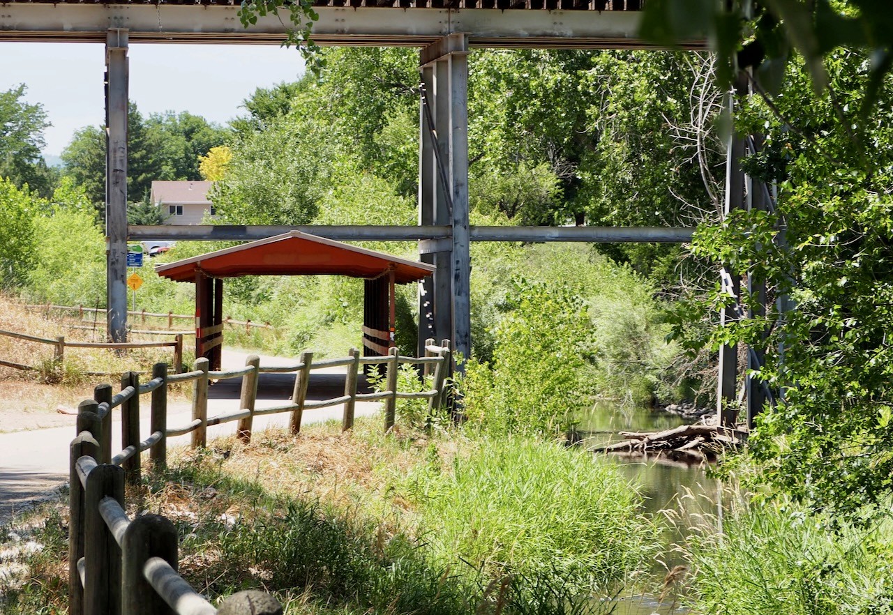 Bike trail next to creek with a shaded wooden underpass.