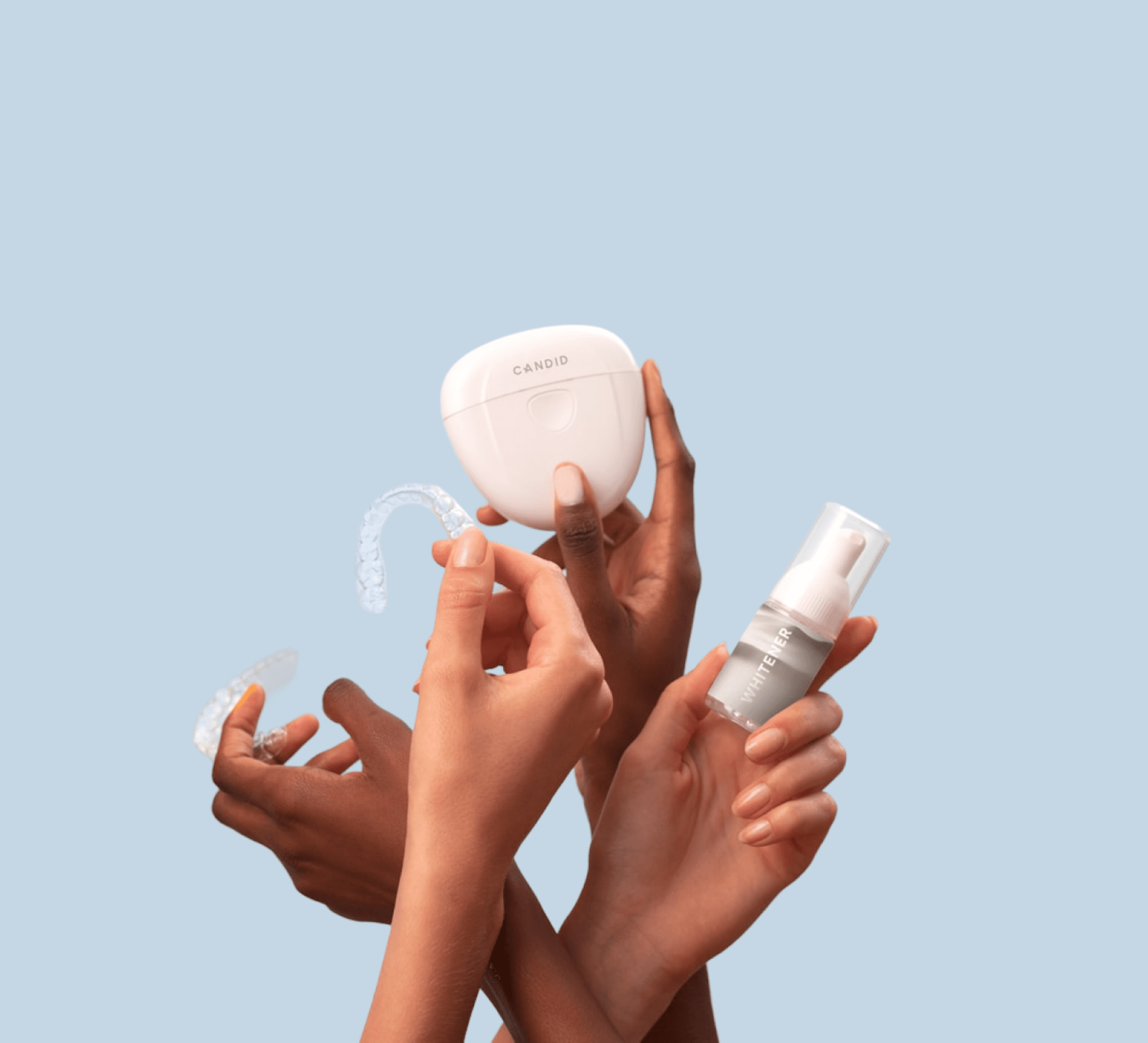 Four hands holding a clear orthodontic aligner, a white storage case, and a small bottle of aligner cleaning solution against a light blue background.