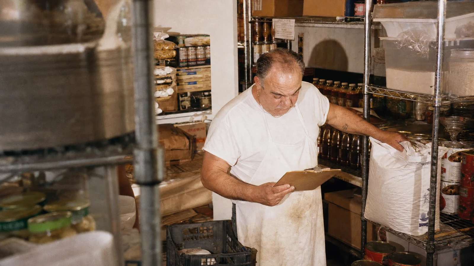 Cuoco spunta l'inventario su un blocco reggendo un sacco di farina nel magazzino