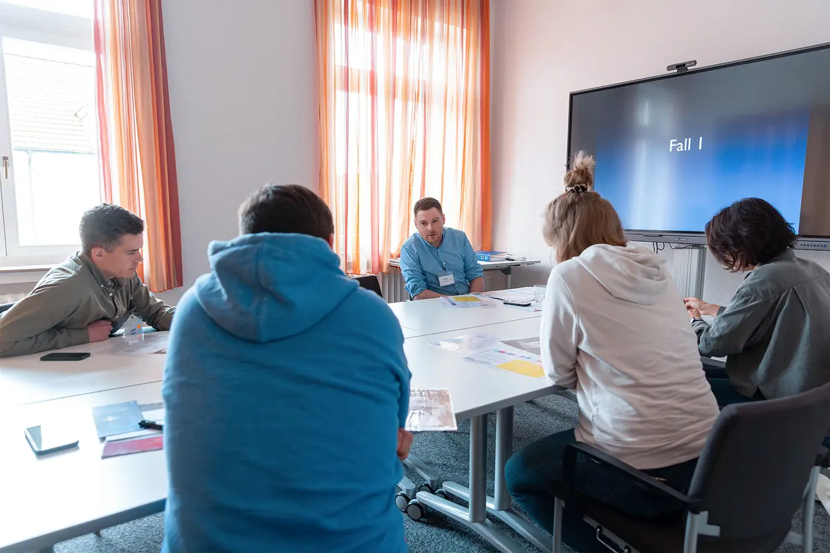 Eine Gruppe von Teilnehmern des SOP Notaufnahme Seminars sitzt locker um einen Konferenztisch in einem hell beleuchteten Raum und schaut gebannt auf einen großen Flatscreen, auf dem „Fall I“ steht.