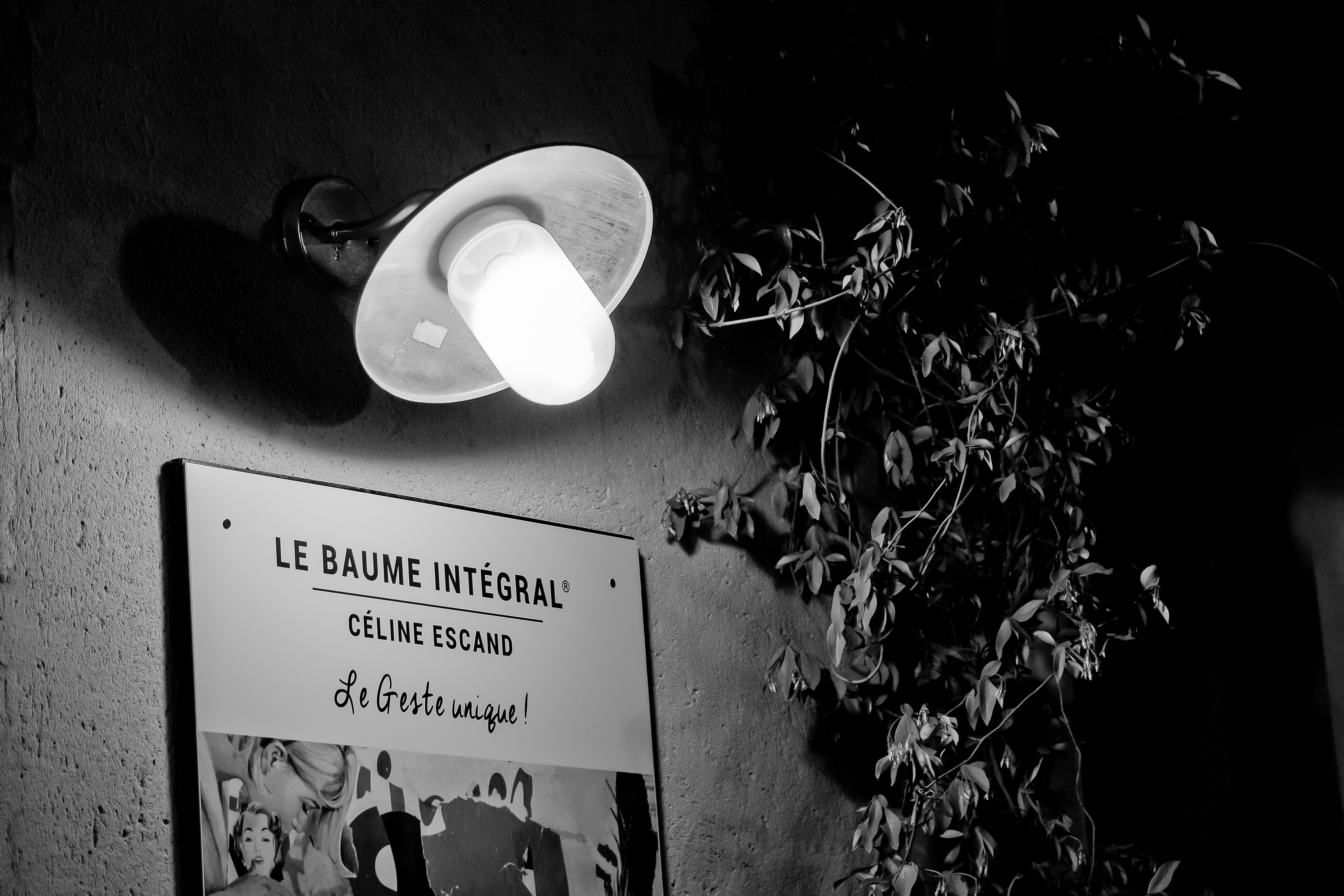 Enseigne du Baume Intégral Céline Escand éclairée par une lampe murale, ambiance nocturne et authentique.