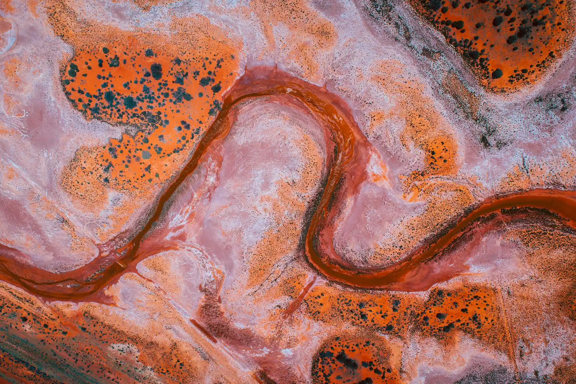 Aerial looking down on an orange salt pan cut by a dark meandering channel