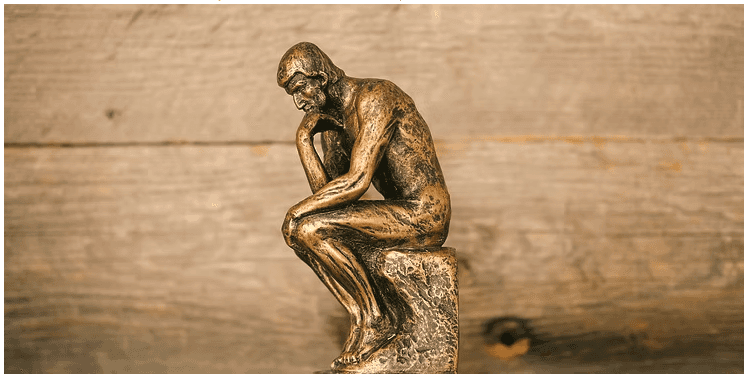 A bronze-colored miniature replica of Auguste Rodin’s sculpture, "The Thinker," positioned against a rustic, light-brown wooden background.