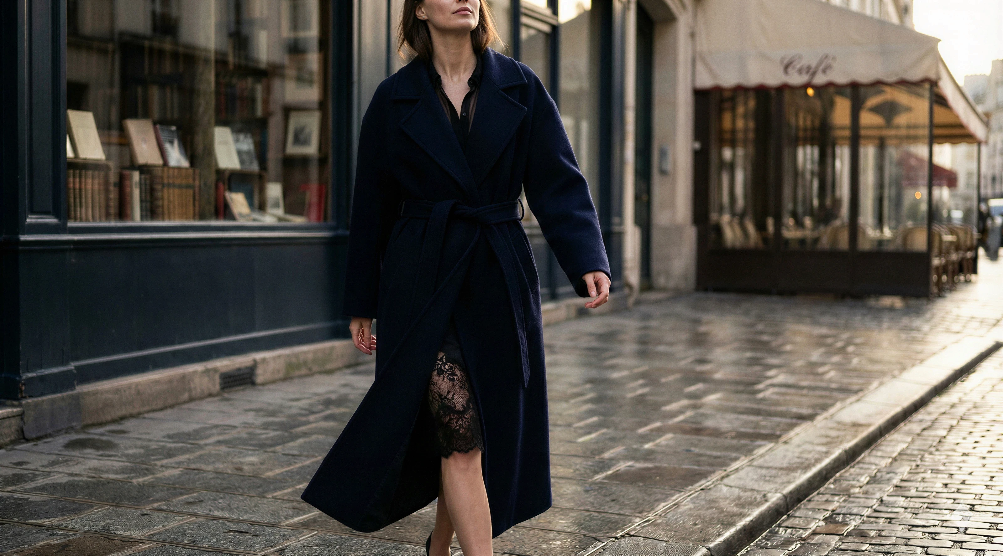Woman in a navy coat walking on a Paris street with a black lace slip visible underneath.