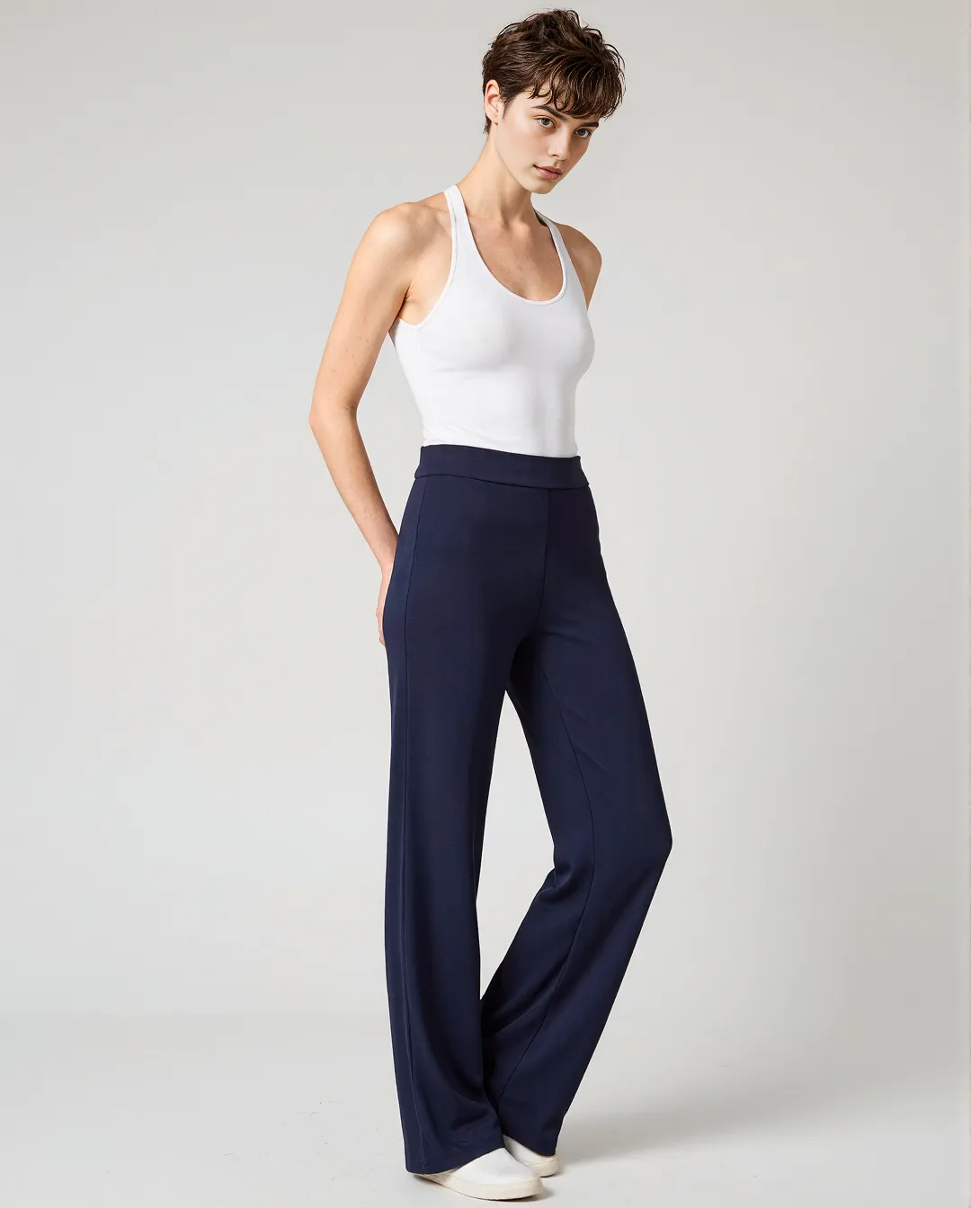 Fashion photography featuring minimalist styling with white tank top and navy wide-leg trousers against neutral background